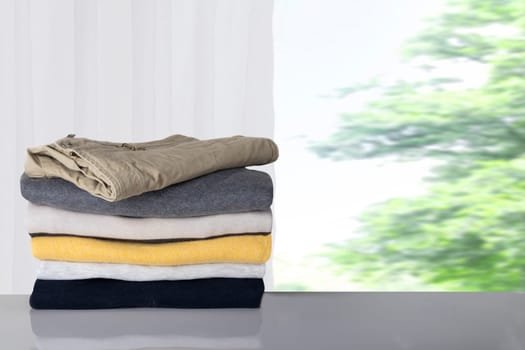 Winter clothes. Stack of colorful cozy warm sweaters and one jeans on table against blurred bright natural background.