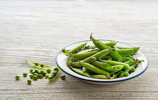 Fresh green peas in a bowl on wooden background