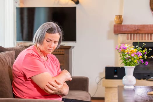 Senior woman suffering from pain in hand at home. Old age, health problem and people concept