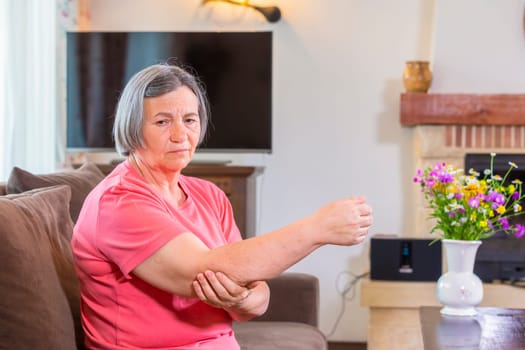 Senior woman suffering from pain in hand at home. Old age, health problem and people concept