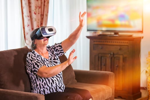 Senior woman with virtual headset or 3d glasses playing videogame at home. Technology, augmented reality, entertainment and people concept. Focus on her hands!