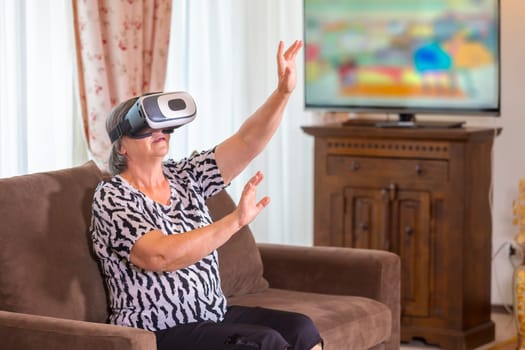 Senior woman with virtual headset or 3d glasses playing videogame at home. Technology, augmented reality, entertainment and people concept. Focus on her hands!