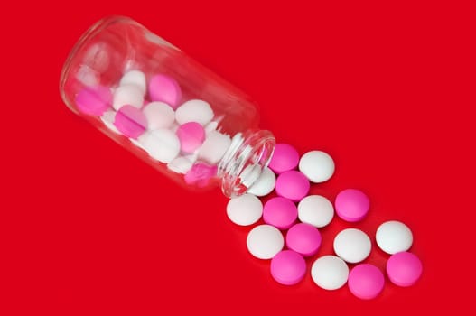 On a red background of a glass bottle scattered white and pink tablets.