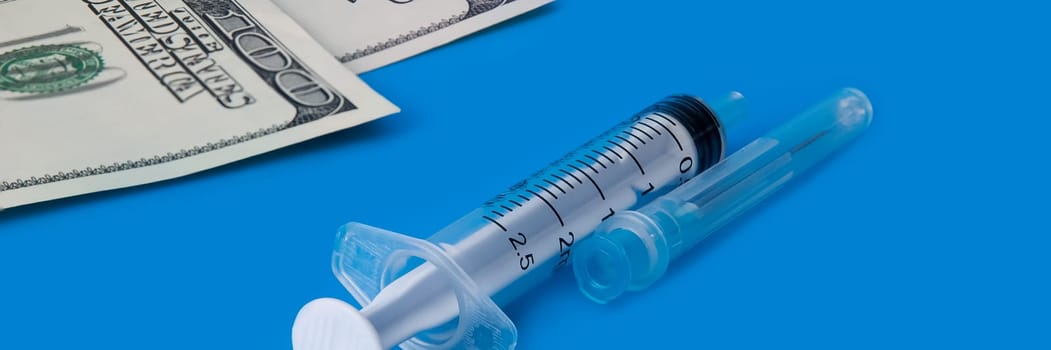 A syringe, and one hundred dollar bills on a blue background.