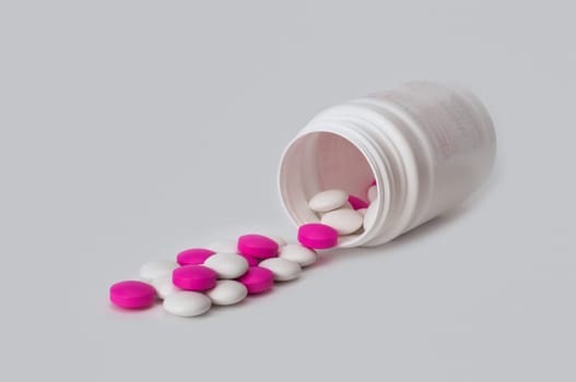 White and white tablets scatter from the white plastic bottle.