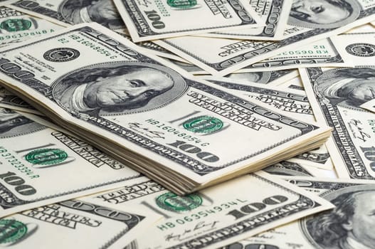A pack of one hundred dollar bills in the background of scattered dollars. View at an angle, from the side.