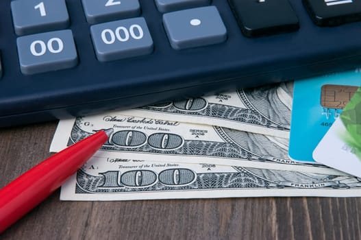 Banknotes for one hundred dollars, credit cards, a calculator and a pen.