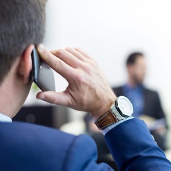 Closeup rear view of successful businessman in a stylish modern navy blue suit holding mobile phone and talking during corporate meeting. Business and entrepreneurship concept.