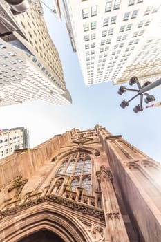 Wide angle upward view of Trinity Church at Broadway and Wall Street with surrounding skyscrapers, Lower Manhattan, New York City, USA.