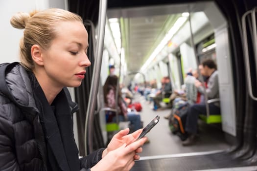 Young girl reading from mobile phone screen while traveling on metro. Wireless internet on public transport concept.