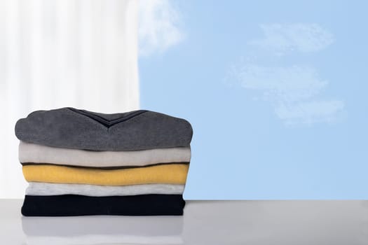 Stack of winter clothes. Pile of colorful cozy warm sweaters against blurred bright background.