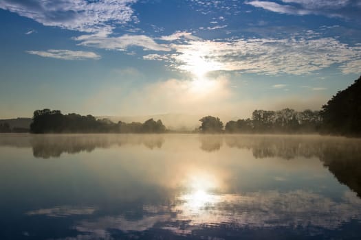 Early summer morning at the pond with a film of mist