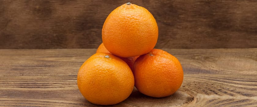 Four mandarins lying down a hill on a wooden table.