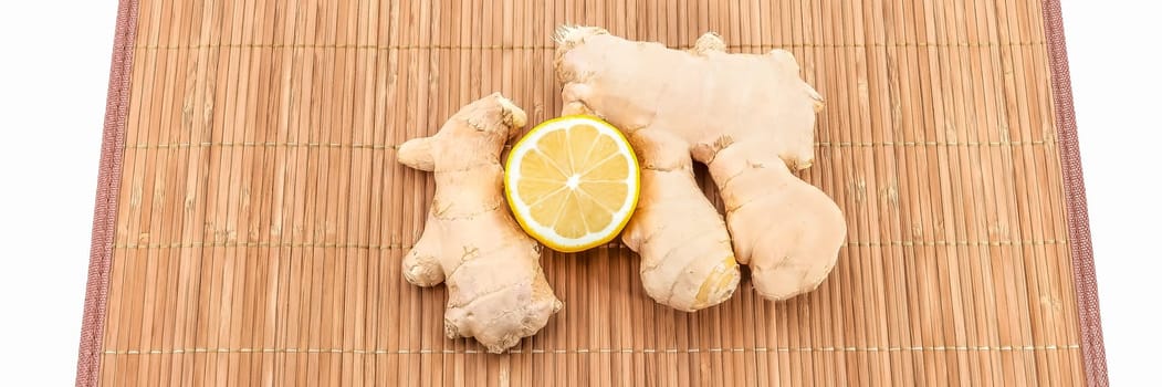 Two pieces of ginger and half a fresh lemon on a bamboo mat.