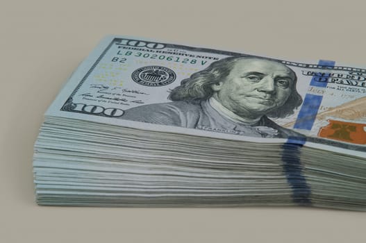 Part of the bundle with a shift of ten thousand dollars in bills of one hundred dollars. On a gray background. View at an angle.