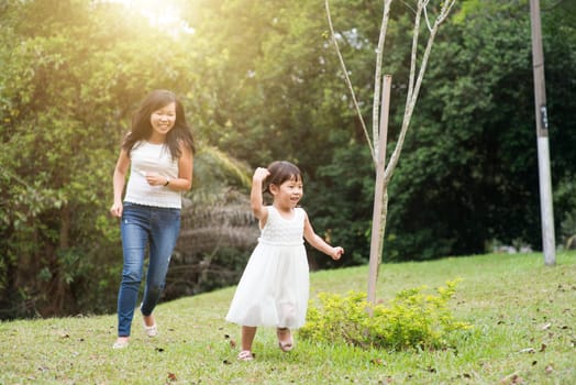 Mother and little girl playing and running at green park. Asian family outdoors activity.