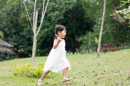 Happy little girl playing and running at green park. Asian family outdoors portrait.