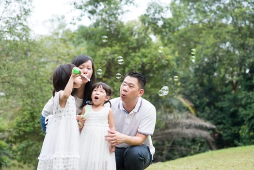 Asian family outdoors activity. Parents and children blowing soap bubbles at garden park.