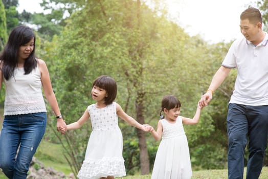 Asian family outdoors. Parents and children holding hands and walking at park.