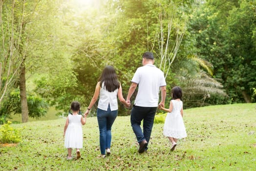 Asian family outdoors. Parents and children holding hands and walking at green park. Rear view.