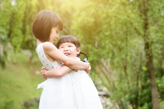 Sisters playing and hugging at garden park. Asian family outdoors portrait.