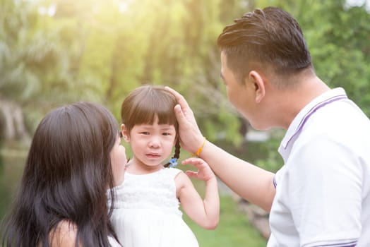 Parents comfort crying daughter at outdoor park. Asian family outdoors portrait.