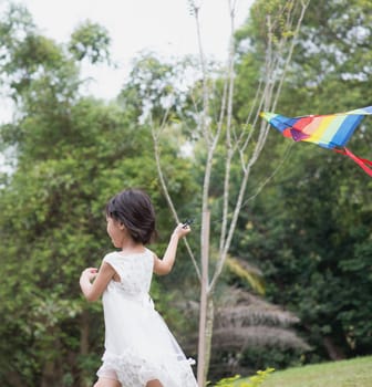 Asian family outdoors activity. Little girl running and flying kite at park.