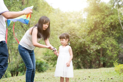 Asian family outdoors activity. Parents and daughter flying kite at garden park.