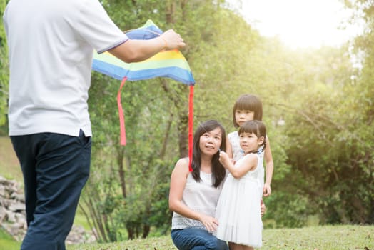 Asian family outdoors activity. Parents and children flying kite at garden park.