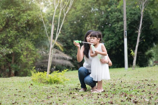 Asian family outdoors activity. Mother and daughter blowing soap bubbles at green park.
