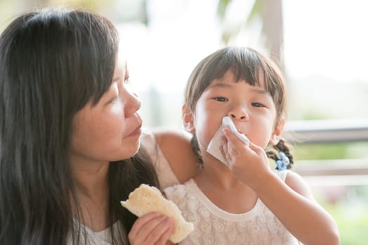Child wiping her mouth at cafe. Asian family outdoor lifestyle with natural light.