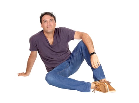 A young slim tall man in jeans and a t-shirt sitting on the floor relaxing.looking at the camera, isolated for white background.