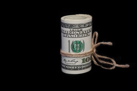 A roll of one hundred dollar bills tied with a rope on a black background. It is located vertically. Side view.