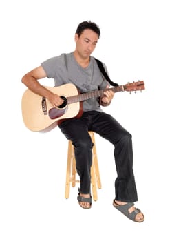 A handsome young man sitting in casual clothing playing his guitar.and singing for himself, isolated for white background.