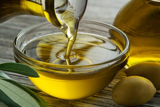 Bottle of virgin olive oil pouring in a bowl close up