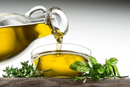 Bottle of virgin olive oil and herbs pouring in a bowl close up