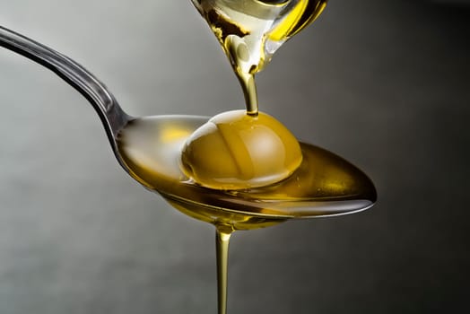 Bottle of virgin olive oil pouring to the spoon close up