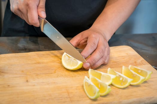 Chef slicing Lemon on wooden cutting board.