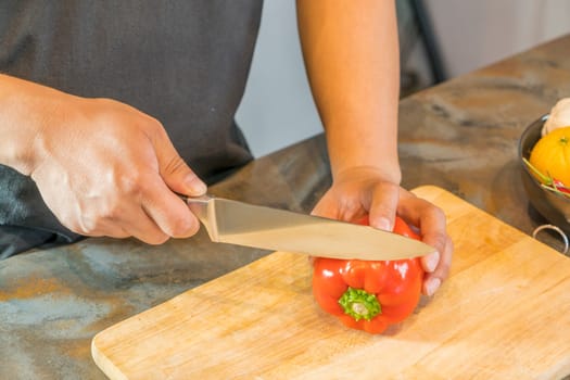 Chef cutting red bell pepper on wooden broad