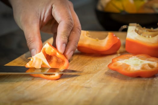 Chef cutting red bell pepper on wooden broad.