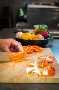 Chef cutting red bell pepper on wooden broad.