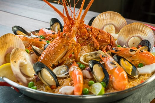 Gourmet seafood Valencia paella with fresh langoustine, clams, mussels and squid on savory saffron rice with prawn, scollops, mussels and lime slices, close up view