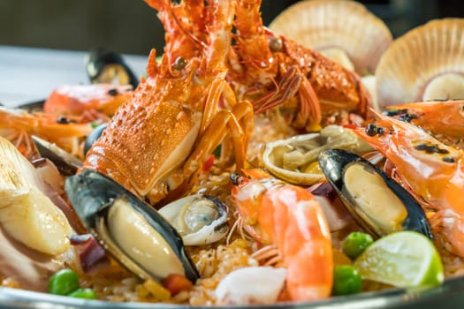 Gourmet seafood Valencia paella with fresh langoustine, clams, mussels and squid on savory saffron rice with prawn, scollops, mussels and lime slices, close up view