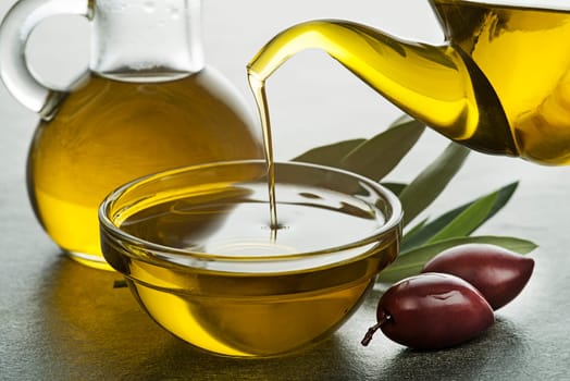 Bottle of Olive oil pouring in a glass bowl with olives