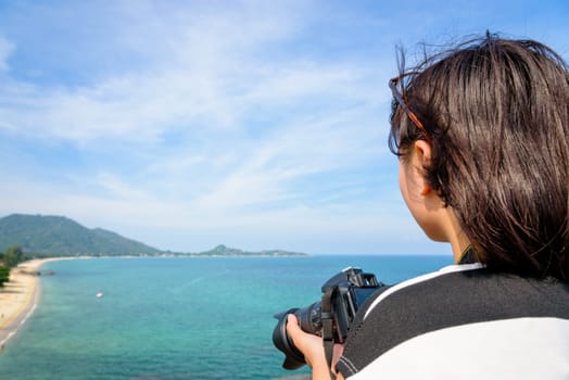 Teenage girl is holding a dslr camera on high and beautiful nature landscape of the blue sea on Lamai beach hight viewpoint during summer travel at Koh Samui island, Surat Thani, Thailand