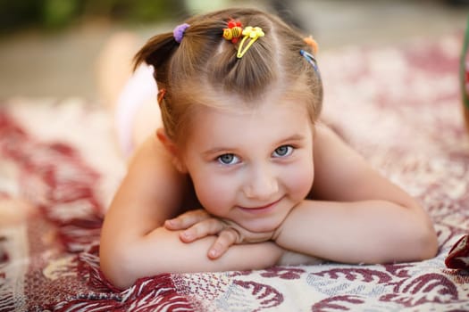Smiling baby girl lying on a blanket outdoors. Child resting. Selective focus.