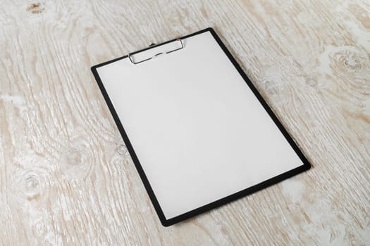 Paper clipboard with blank letterhead on light wooden background with plenty of copy space.