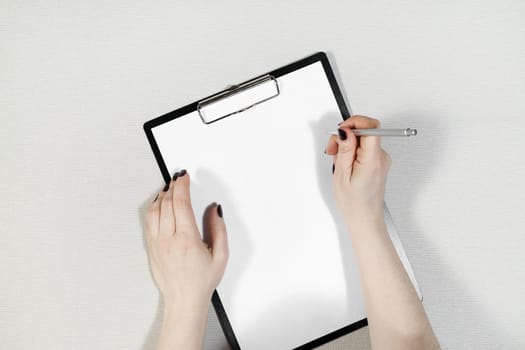 Clipboard with blank paper in female hands. Woman writes. Flat lay.