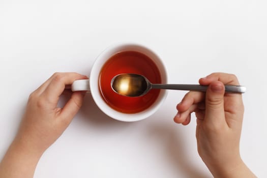 Baby hands with cup of tea and spoon on white background. Tea time.