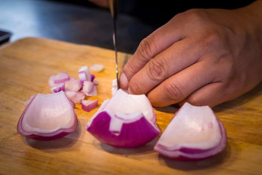 Chef chopping a red onion with a knife on the cutting board.